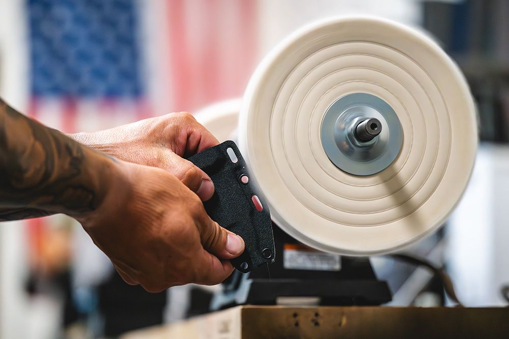 Maker polishing a black Kydex knife sheath on a buffing wheel