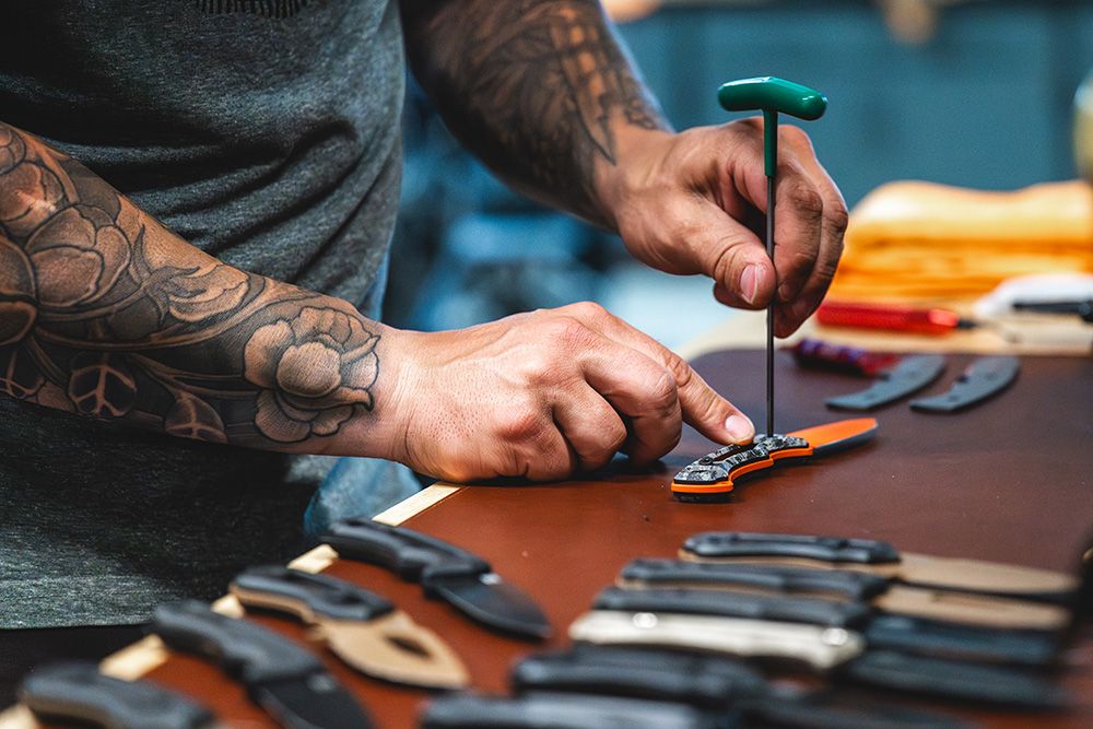 Maker with tattooed forearms assembling a HAViK knife at a workbench