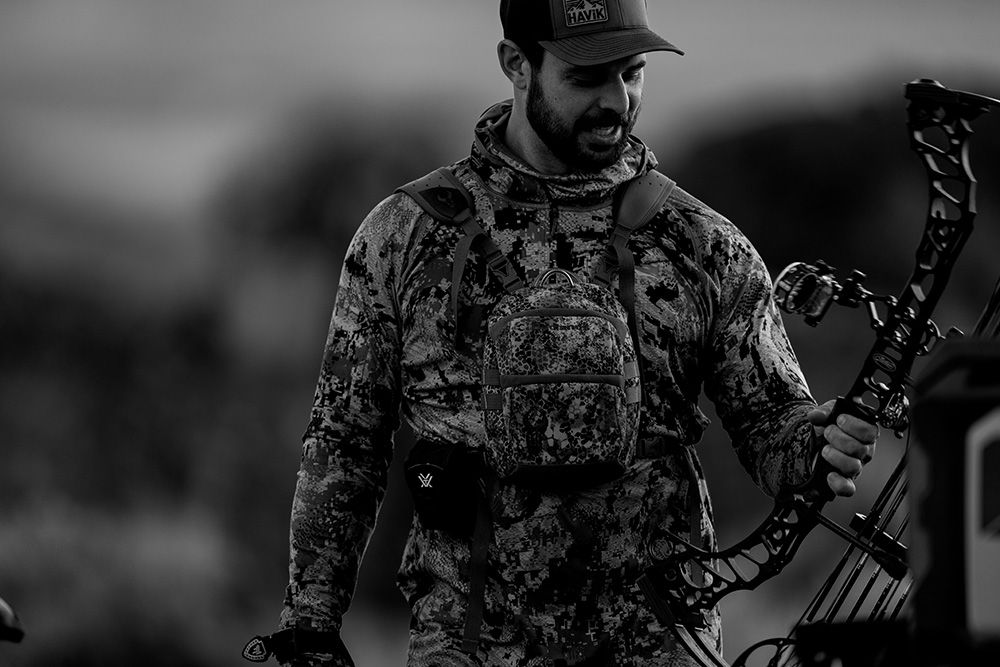 Bowhunter in camo carrying a compound bow in high-desert brush