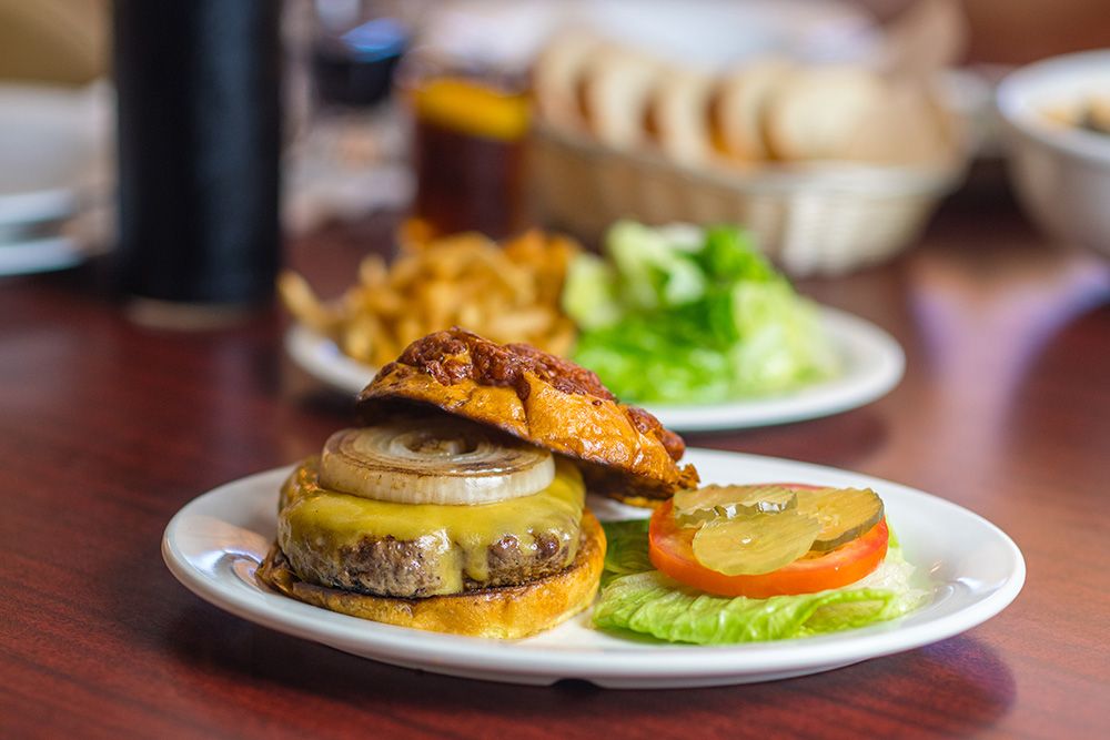 JT Basque cheeseburger with grilled onion and sides on a dark wood table