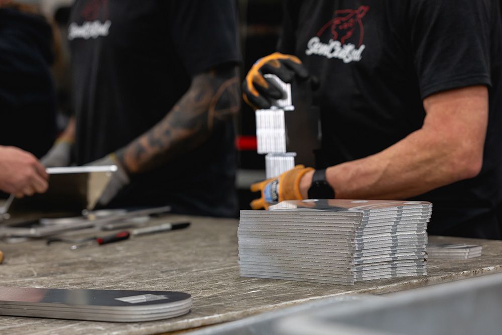 Workers in SendCutSend shirts stacking precision-cut metal plates on a shop workbench