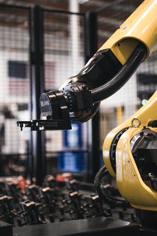 Yellow industrial robotic arm with LANG gripper in a fabrication shop