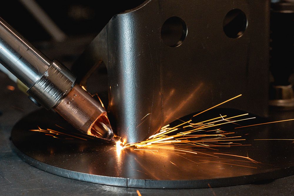Welding torch throwing orange sparks across a circular metal workpiece