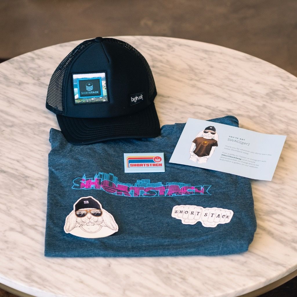 ShortStack promotional swag including a trucker hat, t-shirt, and note card