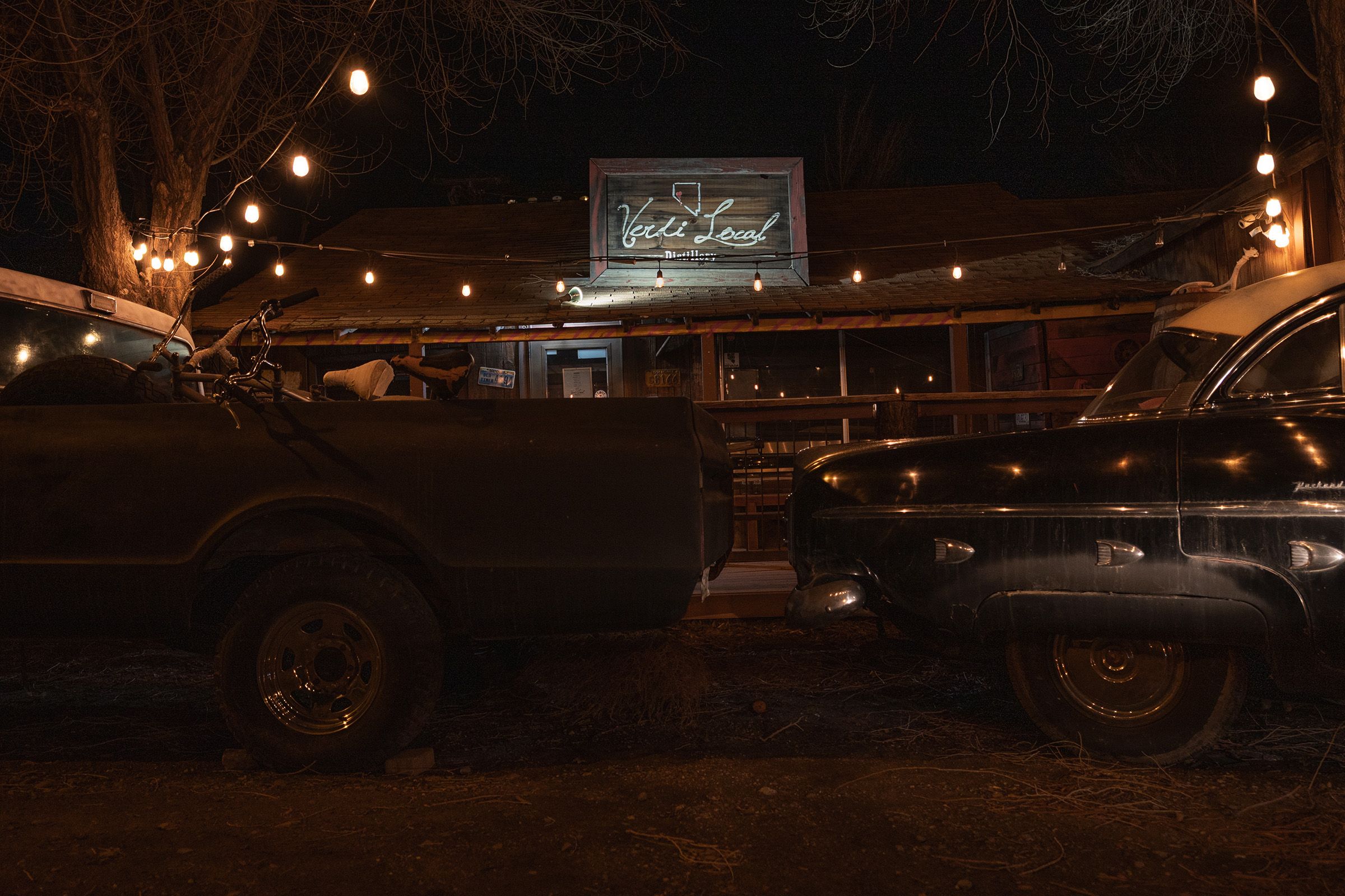 Small-town storefronts at night with wet pavement reflecting neon signs and streetlights