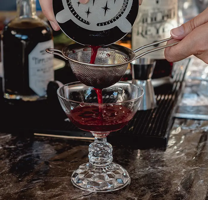 Puuring a blackberry cocktail through a strainer